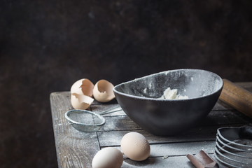 Baking ingredients with bowl of flour, eggs and rolling pin on wooden table