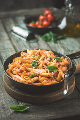 Penne pasta in tomato sauce and cheese decorated with basil on a wooden background