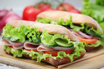 Two sandwiches with fresh vegetables, ham and cheese in ciabatta bread