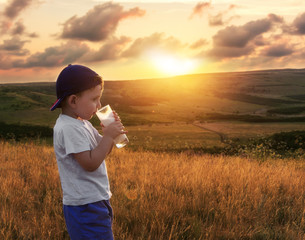 Happy childhood. Cheerful kid is drinking milk at the nature. Scenic view of the meadows and hills.