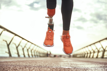 Never give up Cropped photo of disabled woman with prosthetic leg in sportswear jumping on the bridge - obrazy, fototapety, plakaty