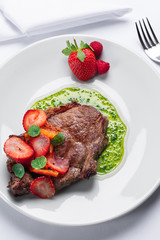 beef stake with strawberry on white dish and basil saus