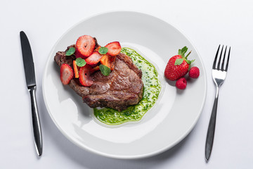 beef stake with strawberry on white dish and basil saus