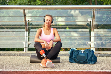 Confident in myself. Portrait of young woman in sports clothing and headphones with leg prosthesis sitting on the bridge and looking at camera