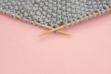 Piece of grey knitted fabric on bamboo wood needles, process of knitting close up on pink background with copy space for text. Top view Flat lay Template for your design