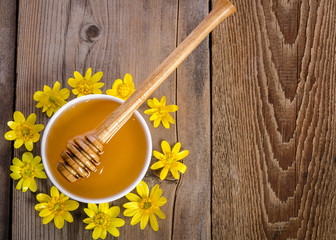 honey in the glass bowl and yellow flowers around it on wooden background