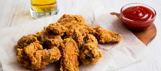 Tasty fried chicken wings with sauce, cold beer on a white wooden surface, side view.