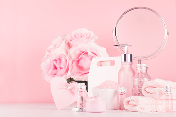 Different skin care products with romantic roses bouquet, round mirror on girlish elegant pink pastel background.