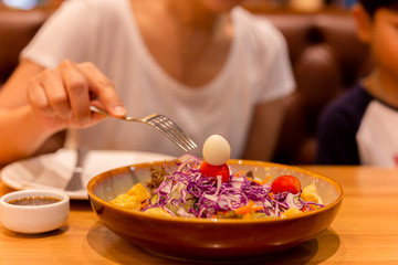 Woman hand with fork eating salad with tomato and quail egg in a plate.