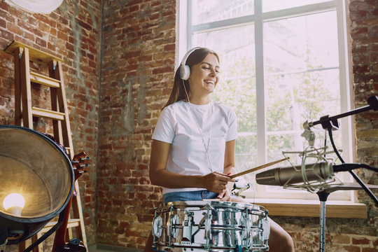 Woman in headphones recording music video blog home lesson, playing drums or making broadcast internet tutorial while sitting in loft workplace or at home. Concept of hobby, music, art and creation.
