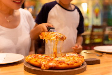 Young boy with mother hand taking a slice of pizza from wooden tray.
