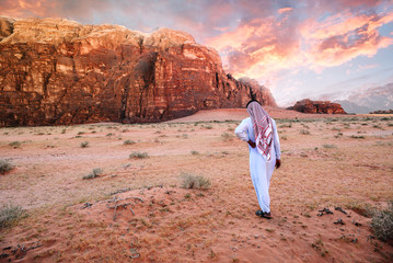 Arabian man in traditiona jordanian clothes (Keffiyeh - traditional Arabic headgear) walking in the wadi-rum desert at sunrise