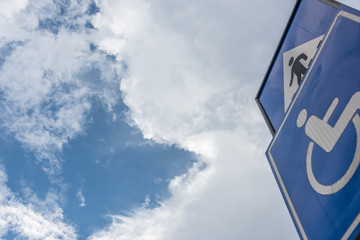 Sidewalk sign with disabled people sign closeup under blue sky white clouds background