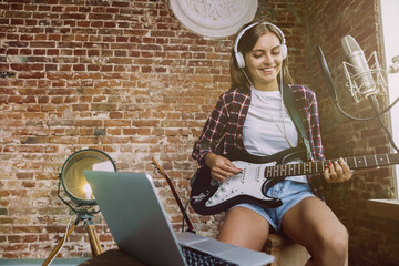 Woman in headphones recording music video blog home lesson, playing guitar or making broadcast internet tutorial while sitting in loft workplace or at home. Concept of hobby, music, art and creation.