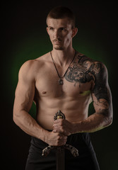 Obraz na płótnie Canvas muscular guy with bare torso posing on a dark background with a sword