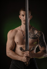 muscular guy with bare torso posing on a dark background with a sword