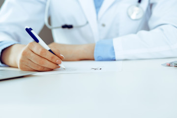 Female doctor filling up prescription form while sitting at the desk in hospital closeup. Healthcare, insurance and excellent service in medicine concept