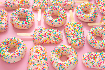 Fototapeta na wymiar festive background of popsicles and donuts with sprinkles and icing over pink background, close up