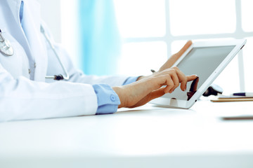 Doctor working table. Woman physician using tablet computer while sitting in hospital office close-up. Healthcare, insurance and medicine concept