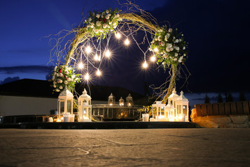 White flowers arch at the wedding ceremony. Outdoors decoration. Romantic rustic style. Lamps...