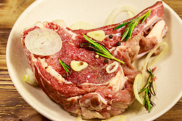 Marinated beef rib eye steak on bone with spices, onion and rosemary on wooden table