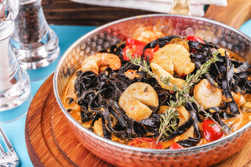Fototapeta na wymiar Mediterranean black pasta with shrimps, tomatoes, dumplings, rosemary and mushrooms