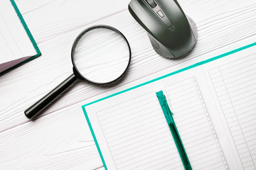 Magnifier and notebook with ballpoint pen and computer mouse on a white wooden table as a concept of search and in-depth research