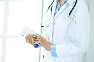 Woman doctor using tablet computer while standing straight in hospital closeup. Healthcare, insurance and medicine concept