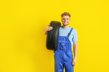 Young male mechanic with car tire on color background