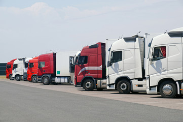 Various types of trucks in the parking lot next to the motorway.