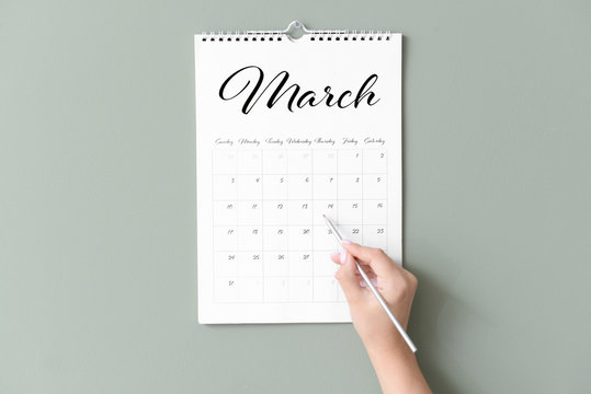 Woman marking date in calendar on color background
