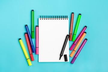 Color markers and a notebook on a blue background. The concept of creativity and education. Back to school. Mock up. Flat lay. Top view. Copy space. Summer time.
