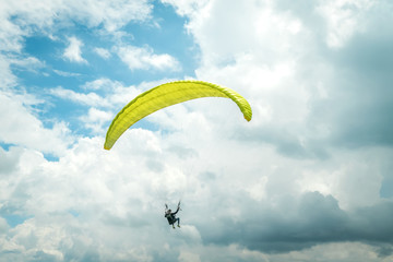 man on a yellow paraglider flying against the sky with clouds on a sunny day. Paraglider is flying...