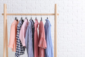 Rack with hanging clothes against white brick wall