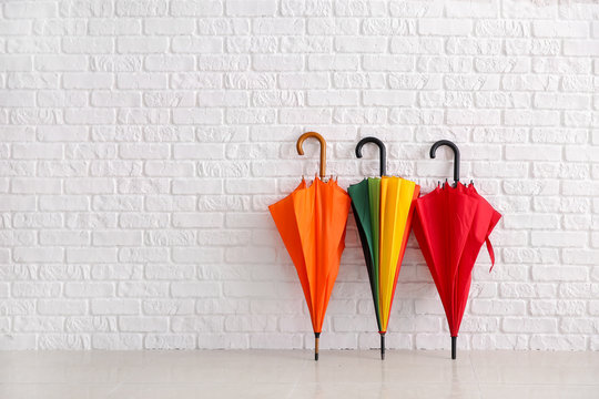 Stylish umbrellas near white brick wall