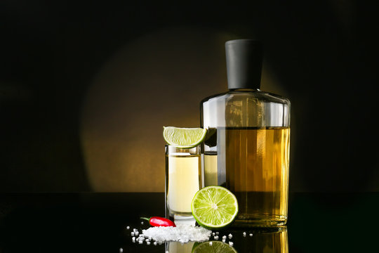 Tasty tequila with lime, salt and chili pepper on dark background