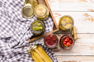 Jars with different canned vegetables, beans and mushrooms on white wooden background