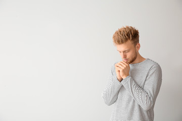 Religious young man praying to God on light background