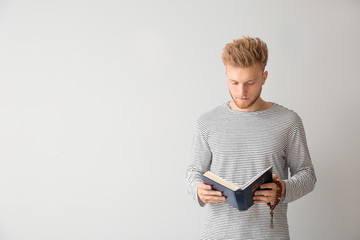Religious young man reading Bible on light background