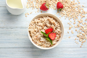Bowl with tasty sweet oatmeal and milk on wooden table