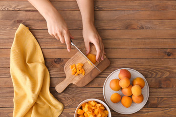 Woman cutting apricots on wooden background
