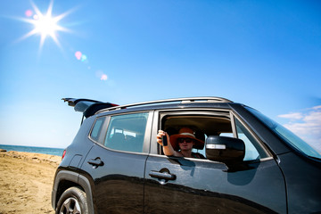 Fototapeta na wymiar A woman in a black car on a sandy beach and blue ocean view.