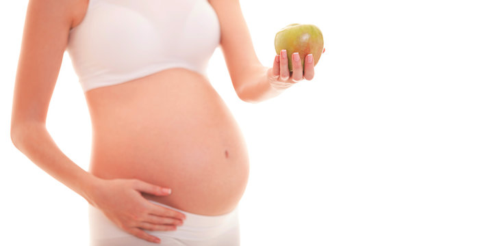 Image of pregnant woman touching her big belly and holding apple in the hand isolated on white background. Close up. Beautiful body of pregnant woman. Motherhood, pregnancy. Woman expecting baby