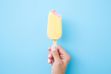 Young woman hand holding pink ice cream with white chocolate glaze on pastel blue background....