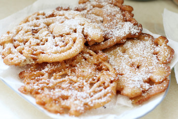 Homemade funnel cakes with powdered sugar on a ceramic plate.