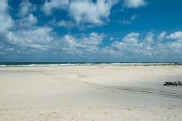 Fototapeta na wymiar White beach sea with white waves under a clear blue sky wit white clouds.