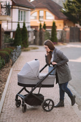 Young mom walking with daughter in stroller. Mother cares for the baby. Mom look in to the stroller and help baby to sleep