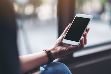 Mockup image of a woman holding white mobile phone with blank desktop screen in cafe