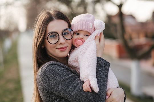 Portrait of mother and her little baby girl. Beautiful mom and cute baby. Mother hud her daughter. Baby dressed in peanch colour hat and nipple toy