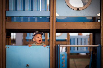 Little boy, child, wearing baseball cap, shouting out loud, standing on a blue playground